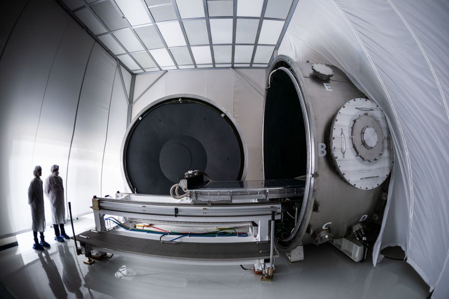 Two technicians standing next to a large thermal vacuum chamber.