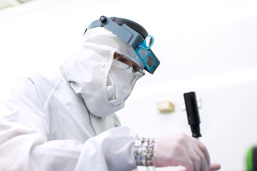 Gowned engineer soldering in a lab.