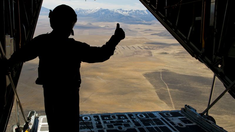 Person standing at the open door of an in-flight cargo plane.