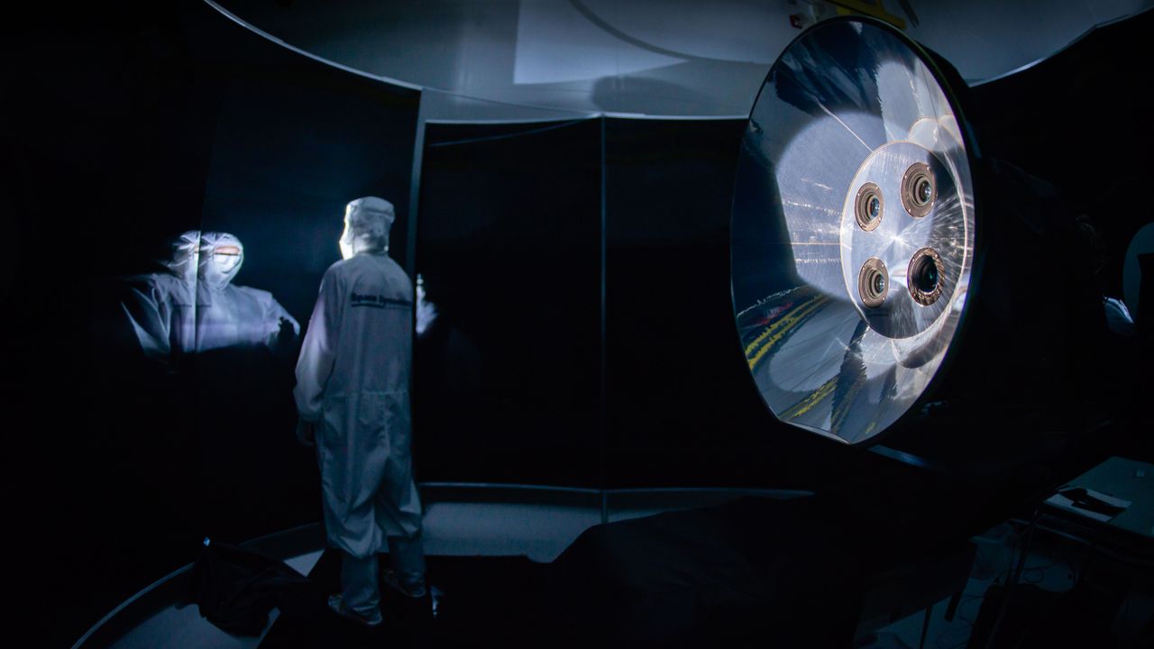 SDL engineer standing next to the Atmospheric Waves Experiment (AWE) telescopes, with baffle, in a stray light test facility.