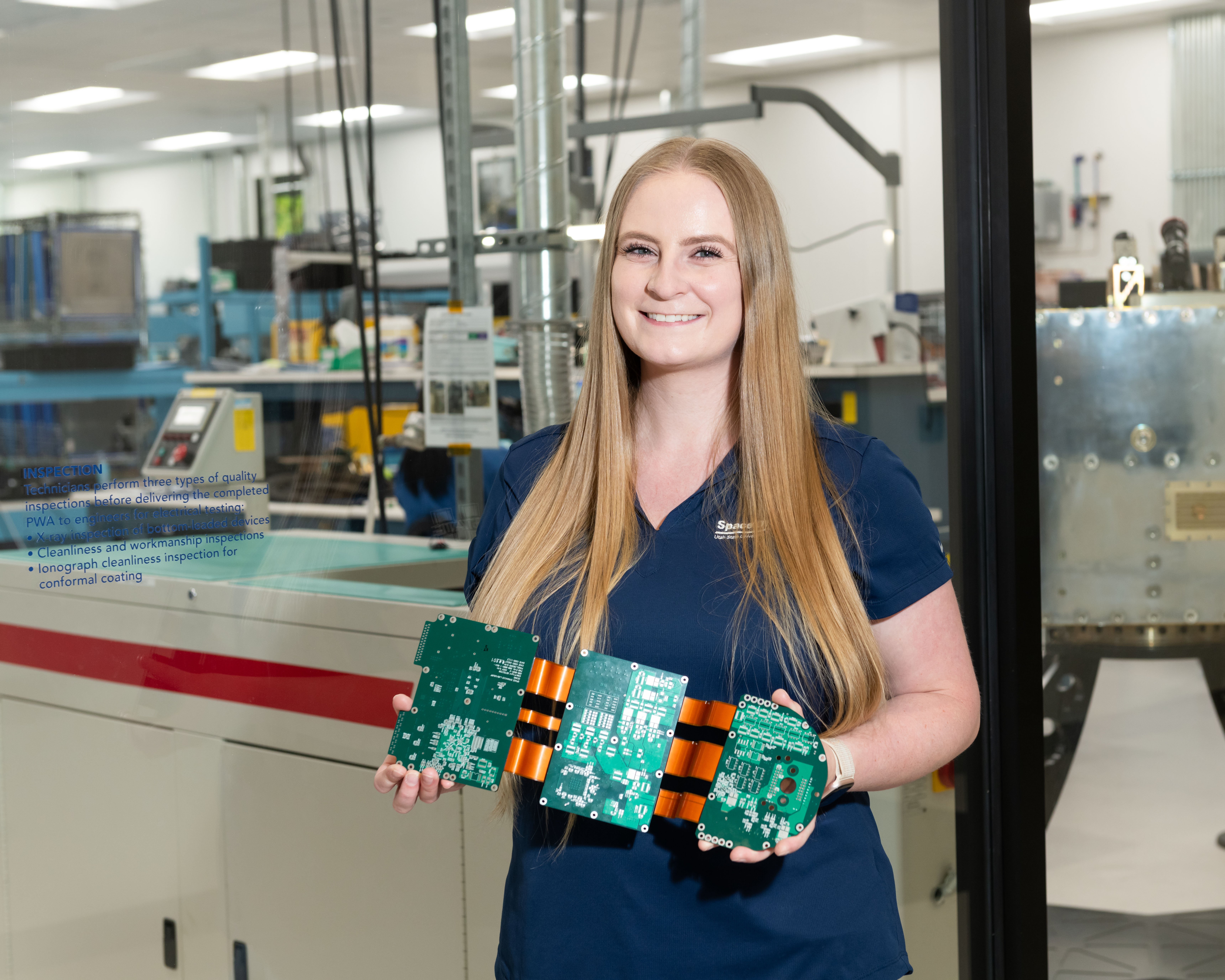 Ashley Roth standing in front of a laboratory holding a piece of hardware.