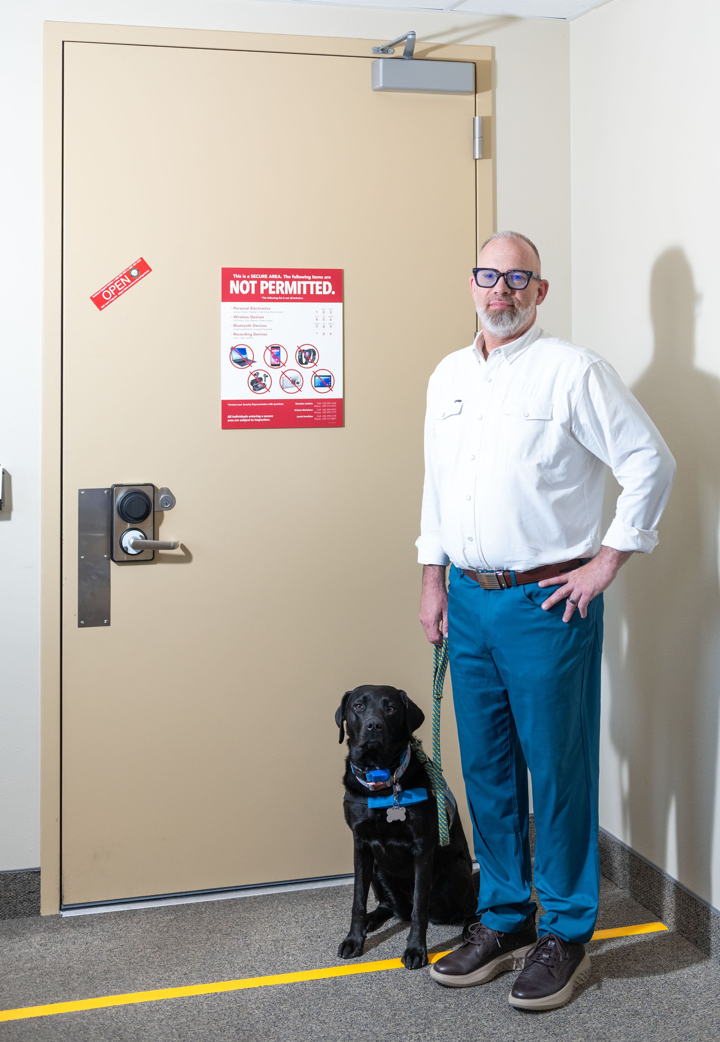 Kory Kelly standing in front of a secure room door with his service dog.