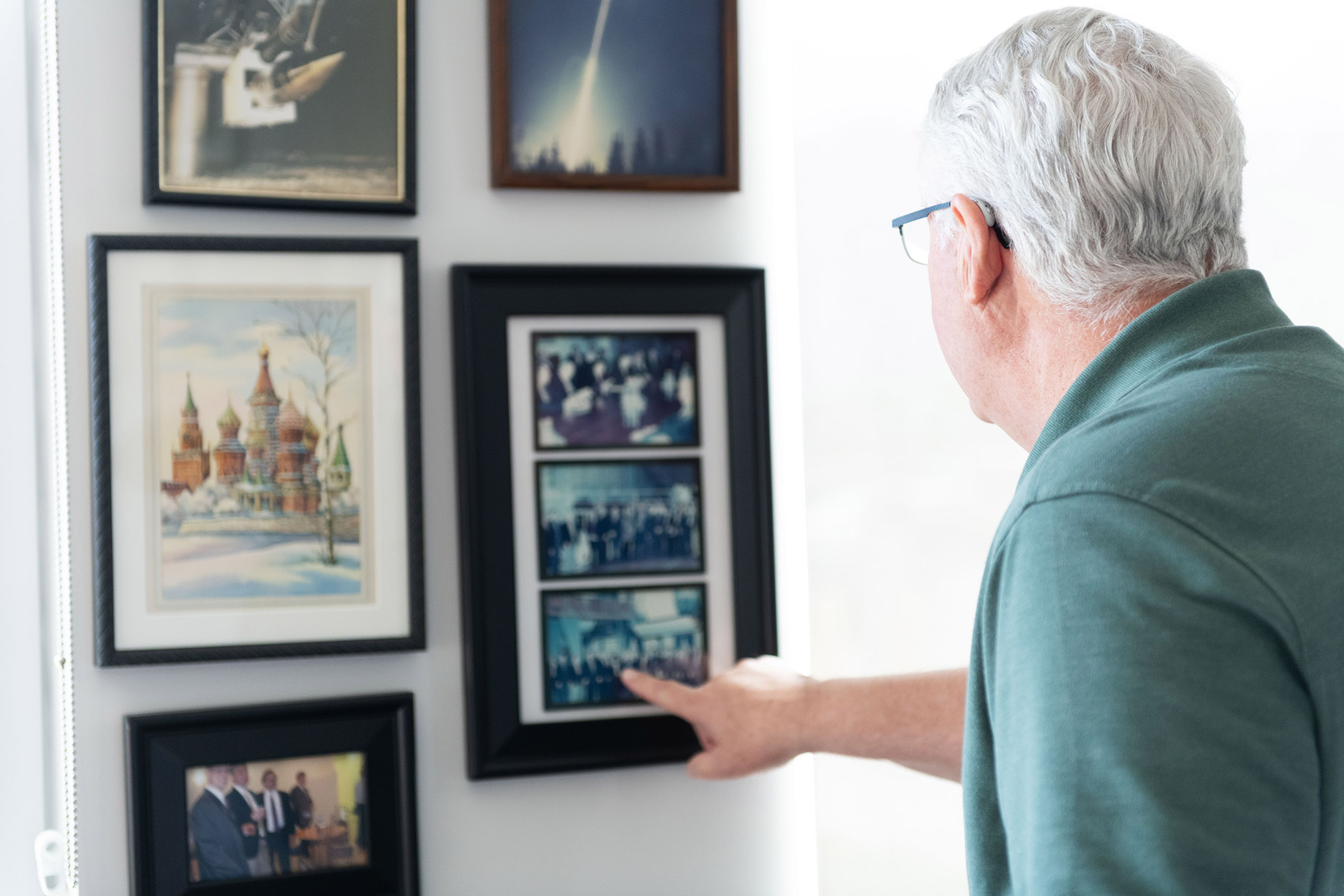 Kirk Larsen pointing to a wall of framed program photographs.