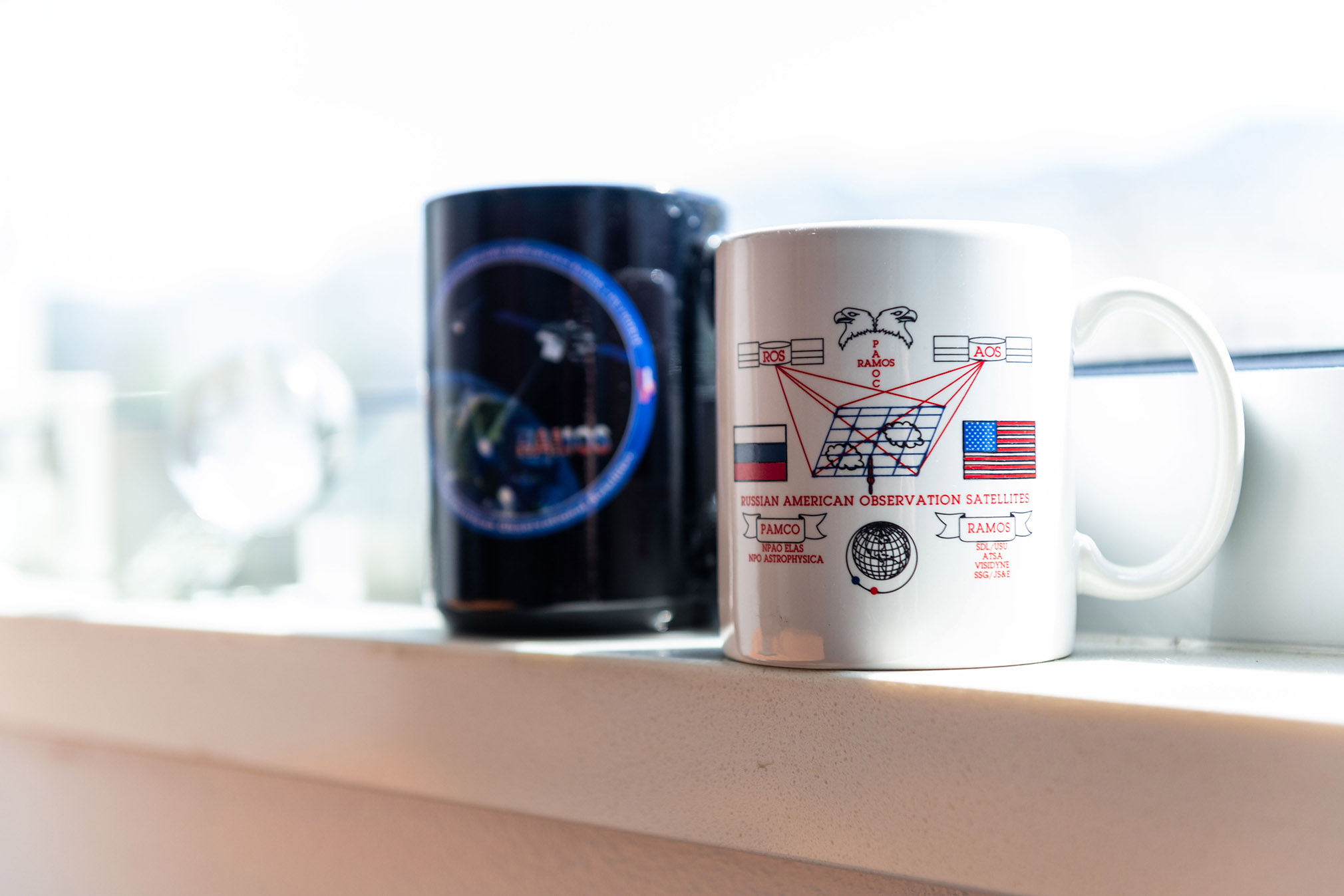 Mission memorabilia and two commemorative mugs resting on a windowsill.