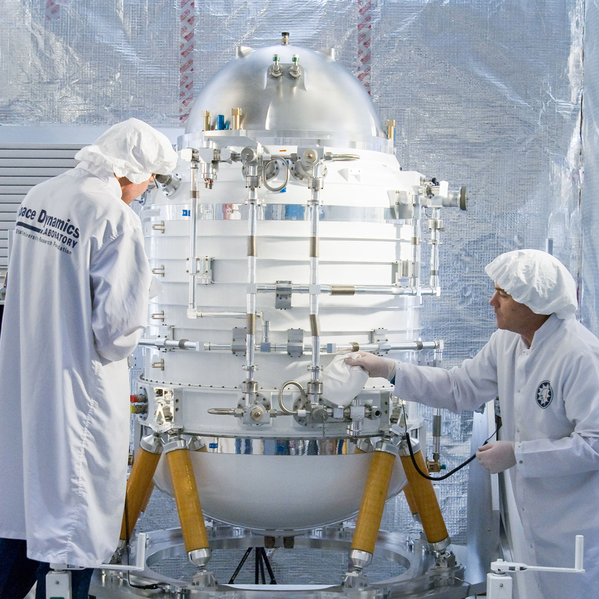 Two employees in protective suits working on the Wide-field Infrared Survey Explorer (WISE) science instrument inside an SDL cleanroom.